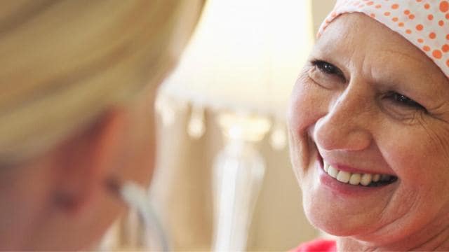 Eine Frau mit gepunktetem Kopftuch lächelt, während sie einer anderen Person gegenübersteht. Im Hintergrund ist eine brennende Lampe zu sehen.