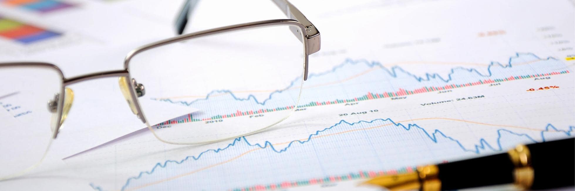 Die Brille liegt auf einem Blatt Papier, auf dem Finanzdiagramme und -grafiken abgebildet sind. Daneben liegt ein Stift.