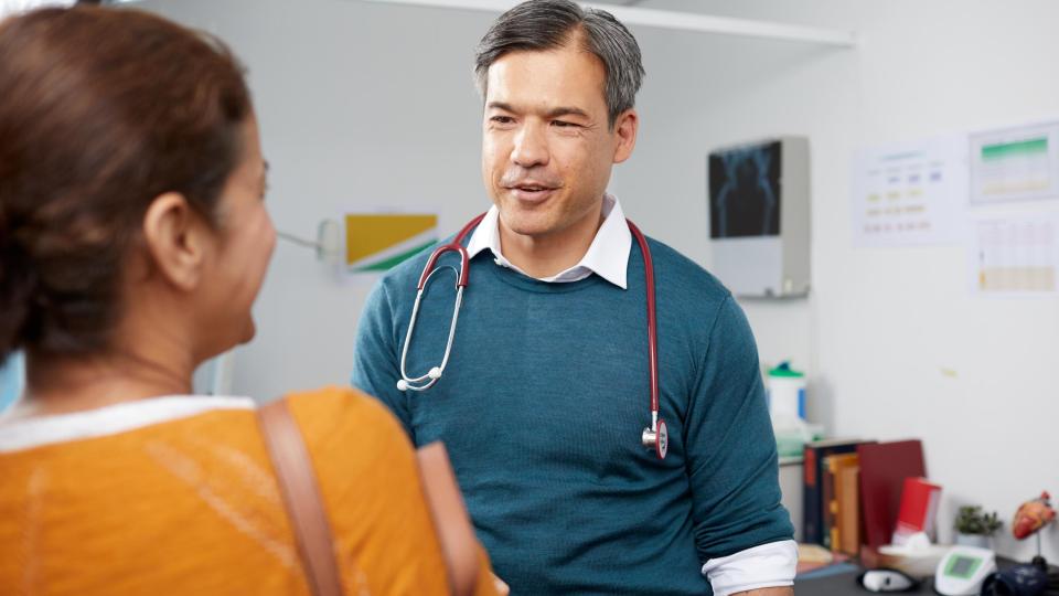 Ein Arzt mit einem Stethoskop spricht mit einem Patienten in einer Arztpraxis.